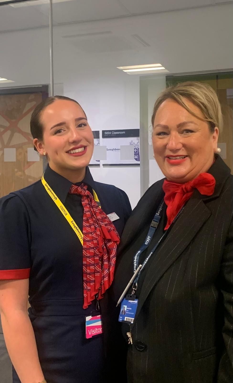 Remi poses with her former lecturer Deborah. Remi is on the left and wearing her Cabin Crew uniform and a visitor lanyard. Deborah is on the right and is wearing a black jacket and red scarf. They are both smiling at the camera.