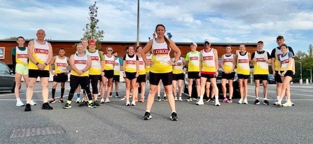 Sheree stands in front of her running club. They are all wearing yellow running vests.