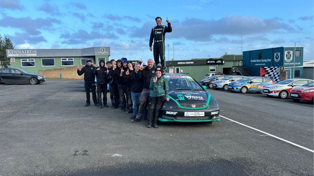 Alex Fletcher stands on the car. Next to the car, the rest of the Loughborough College team of students and teachers celebrate