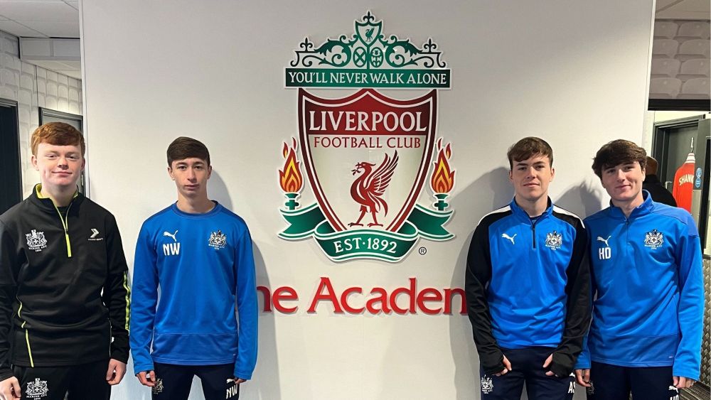 Four HND students stand next to the Liverpool Football Club Academy Crest.