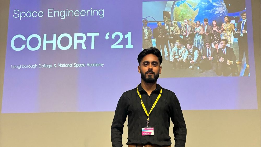 Alumni Moiz stands in front of a screen that reads 