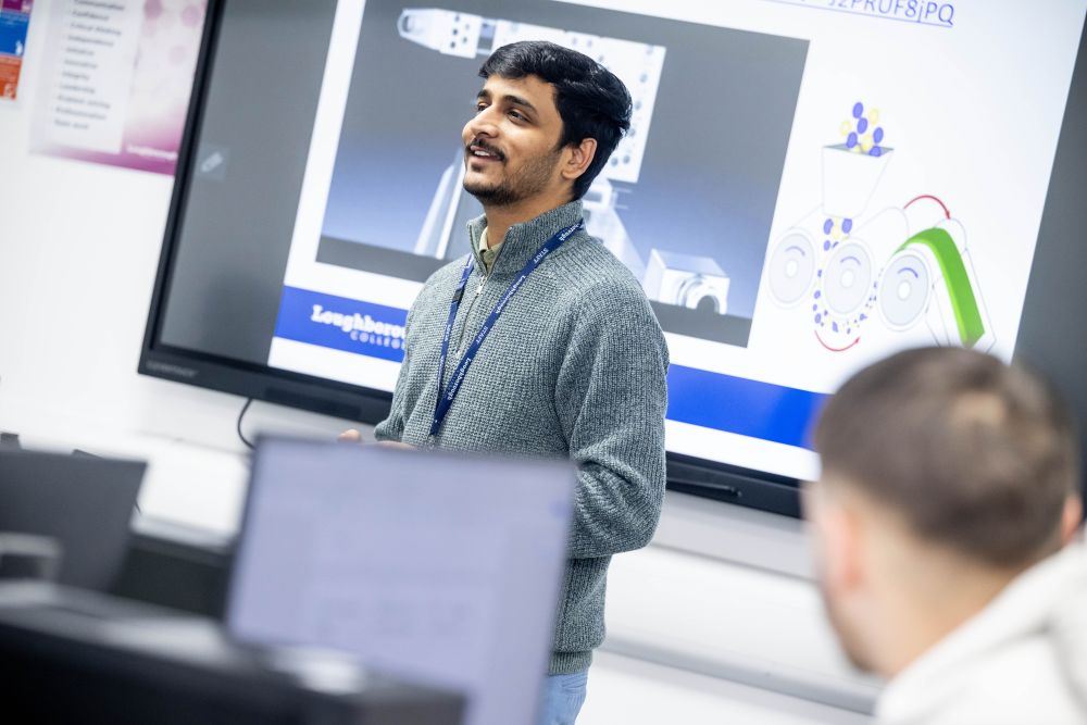 A lecturer stands in front of a digital whiteboard